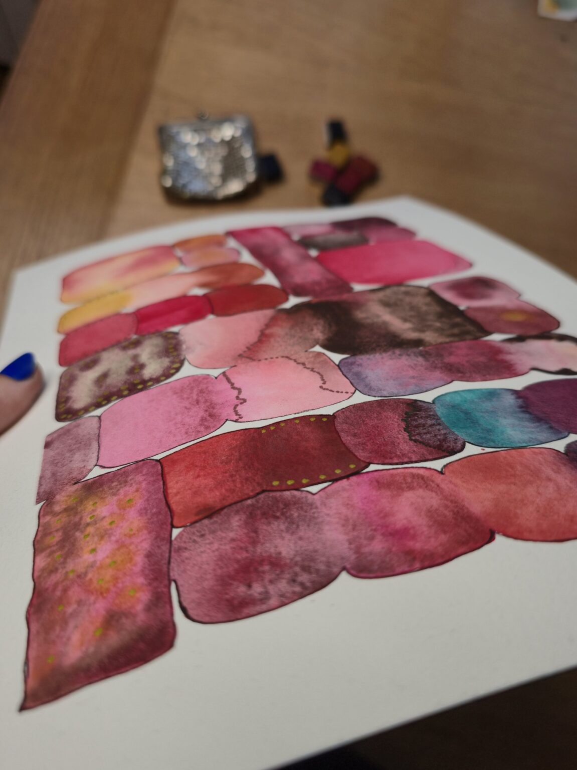 Nuancier d'aquarelles roses peint à la main, avec le porte-monnaie en maille métallique et les demi-godets en arrière-plan – Madame Pigmentum