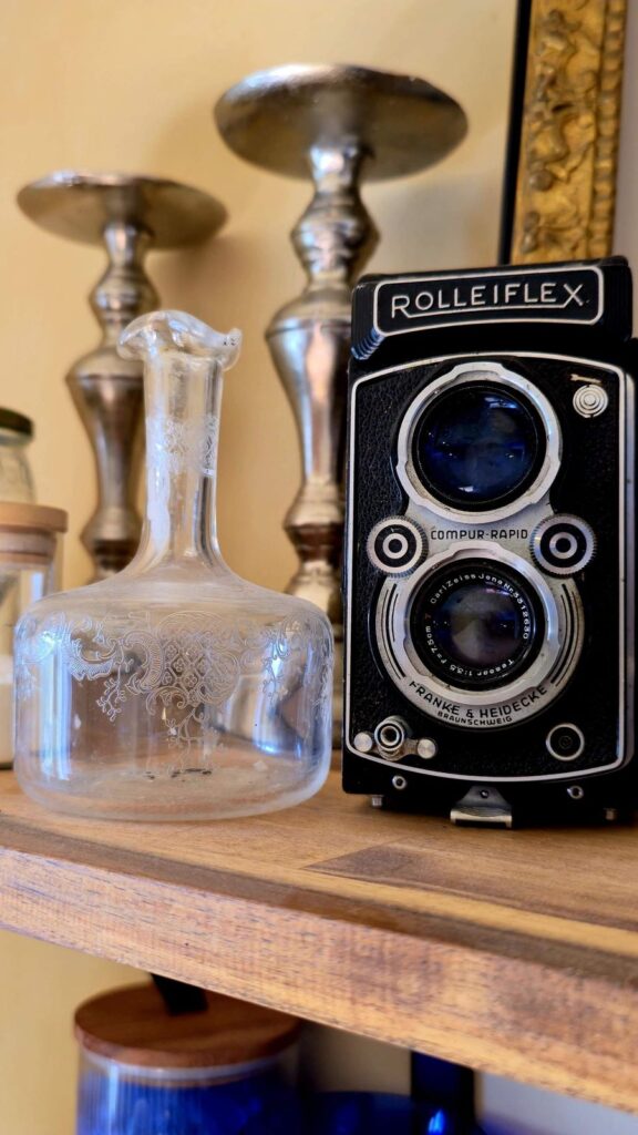 Carafe en verre gravé, appareil photo Rolleiflex et bougeoirs sur une étagère